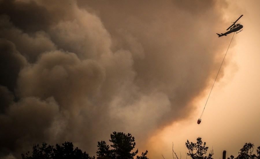 a helicopter flies in a sky filled with smoke over fires in australia