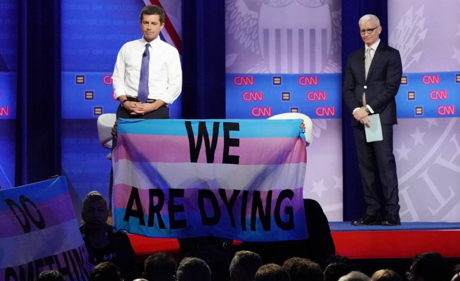 Democratic presidential candidate South Bend, Indiana Mayor Pete Buttigieg (L) and CNN moderator Anderson Cooper react as protestors display banners at the Human Rights Campaign Foundation and CNN’s presidential town hall focused on LGBTQ issues on Octobe