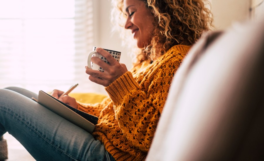 a woman sits alone on the couch with a mug and a book