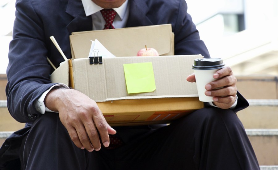 a man sits on stairs with a box of belongings after being laid off