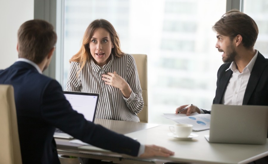 a man points at a woman who looks shocked as they sit in front of a higher up