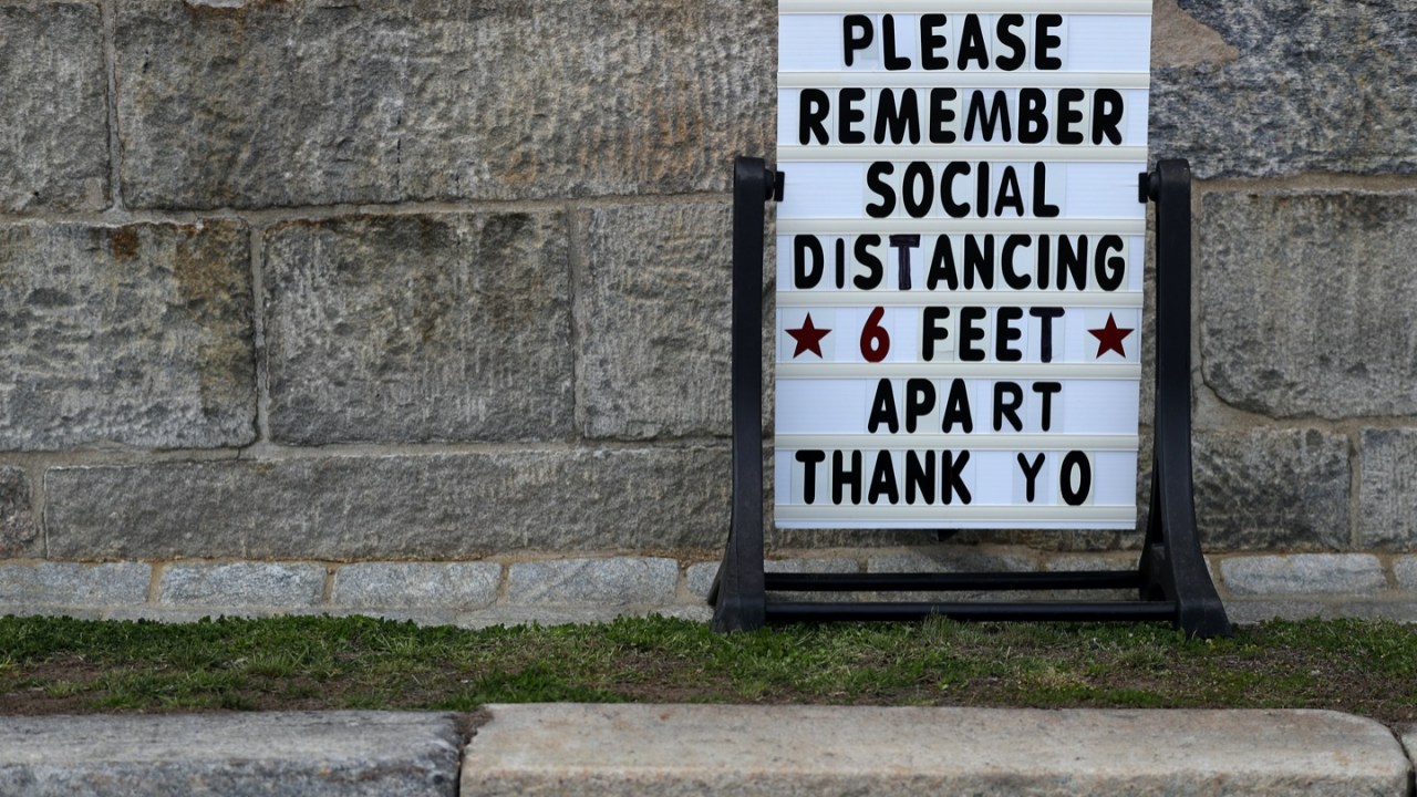 a sign outside a store reminds people to practice social distancing and stay 6 feet apart