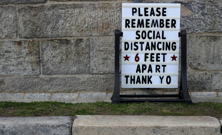 a sign outside a store reminds people to practice social distancing and stay 6 feet apart