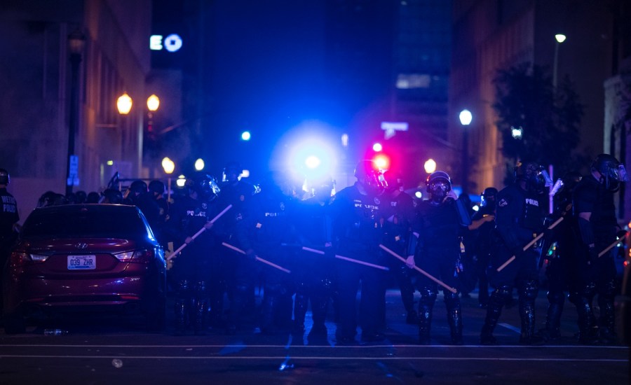 police lights and a line of police officers in riot gear at night in Louisville, Kentucky