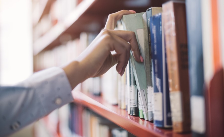 a hand pulls a book out of a shelf at a library