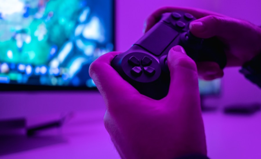 Closeup hands of anonymous male holding modern controller while playing video game in dark room