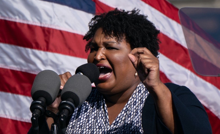 stacey abram speaks with an American flag behind her