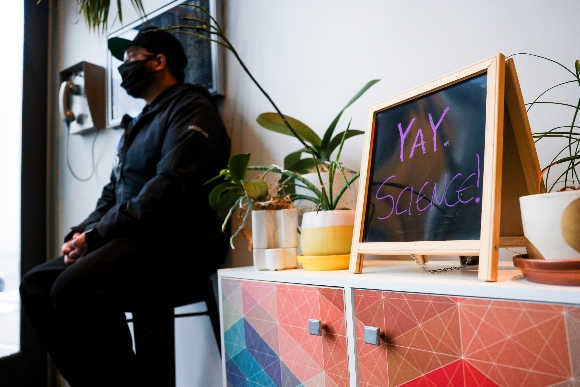 Bar Max doorman Edric Sanchez sits behind a sign reading, Yay science