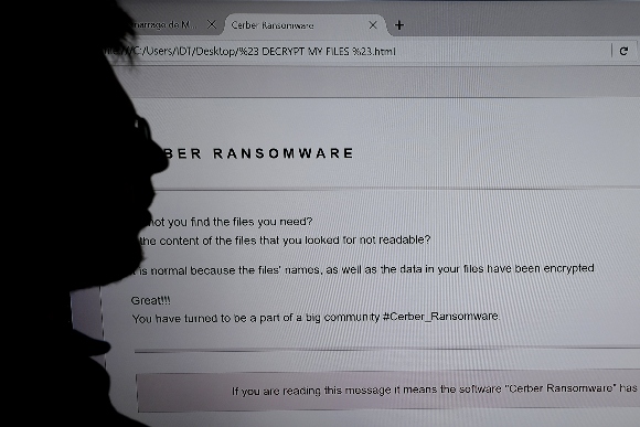 An IT researcher stands next to a giant screen displaying a computer infected by a ransomware