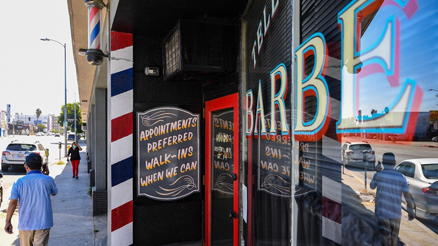 A man walks past a barbershop with a sign that reads "Appointments preferred walk-ins when we can"