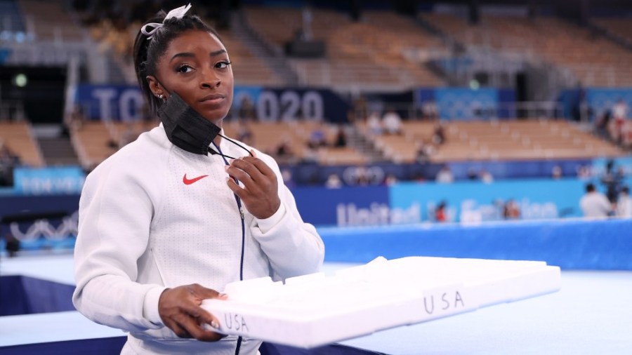 Simone Biles of Team USA supports her gymnastics teammates by carrying their chalk