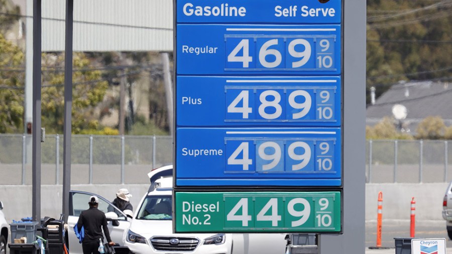 Gas prices on a blue board are seen at a California gas station with cars getting gas in the background