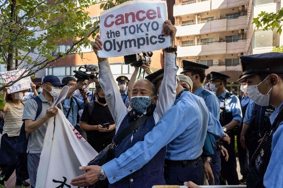 Police officers block a protester as they walk towards the hotel where International Olympic Committee president Thomas Bach is staying for a demonstration in Tokyo