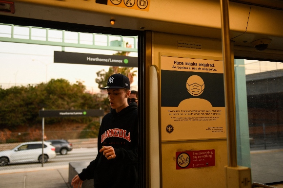 Face mask signage is displayed as a transit passenger boards the Metro C Line, formerly Green Line, light rail train alongside the 105 Freeway during rush hour traffic in Los Angeles