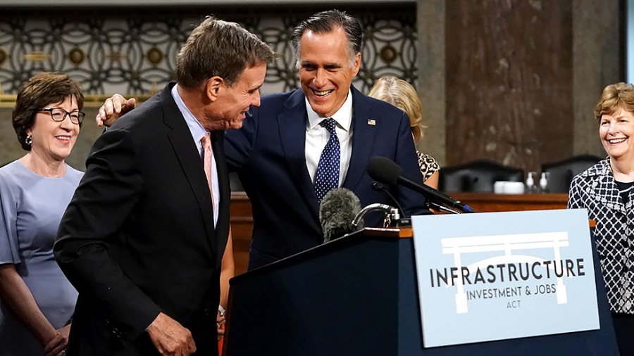 Sen. Mark Warner (D-Va.) hugs Sen. Mitt Romney (R-Utah) as they addresses reporters after a key vote regarding bipartisan infrastructure legislation on Wednesday, July 28, 2021.