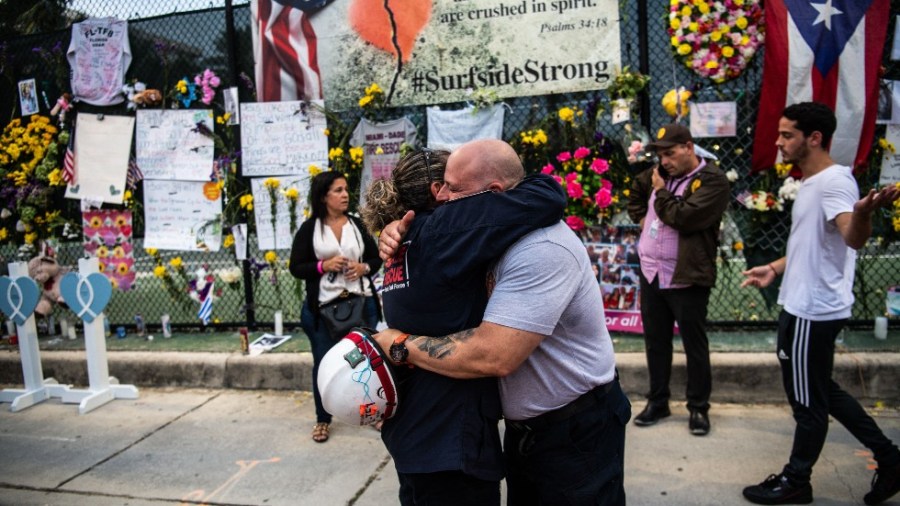 Members of Miami-Dade Fire Rescue hug each other at the "Surfside Wall of Hope & Memorial"