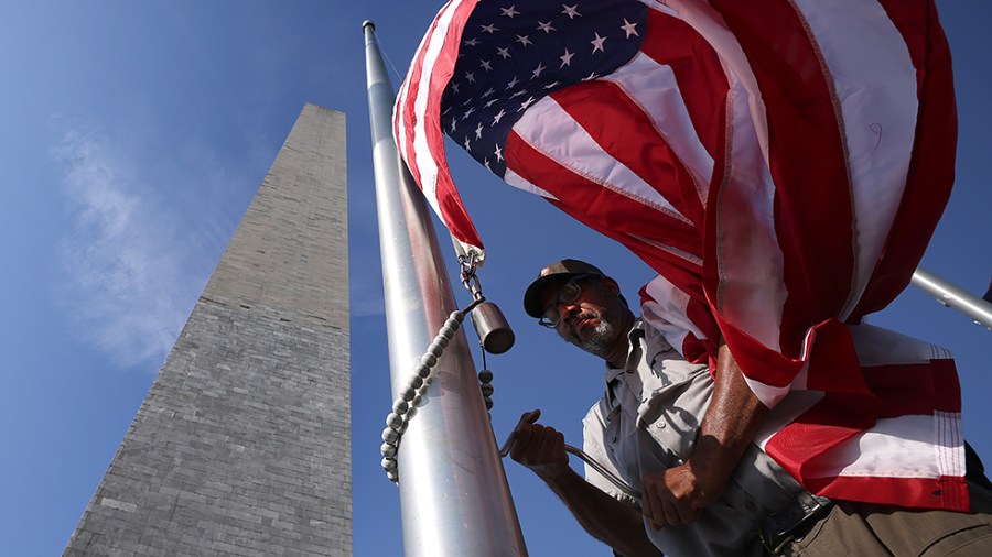 U.S. Park Service employee Ronald Lewis replaces a worn flag as the Washington Monument reopens on July 14, 2021. The Washington Monument has been closed for the last six months due to the COVID-19 pandemic