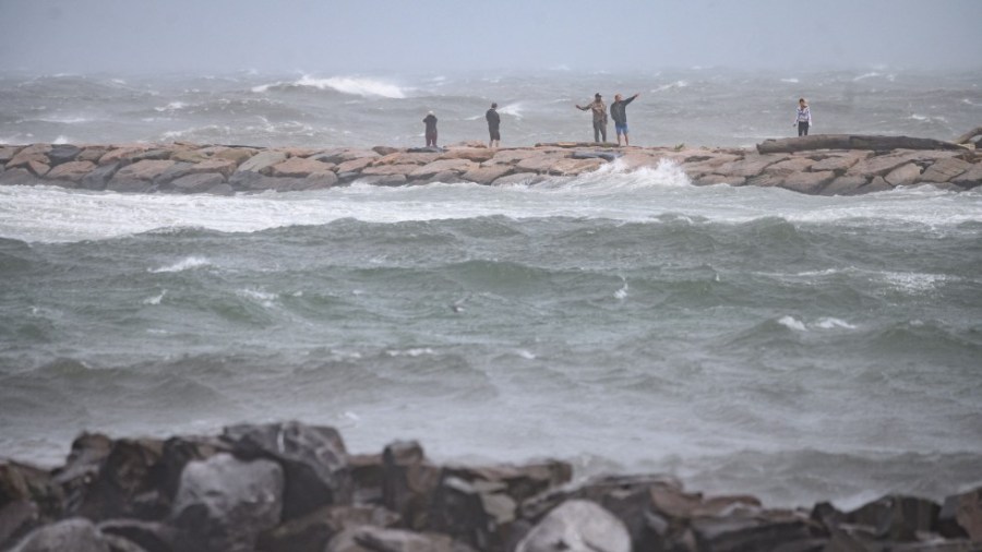 People watch the waves as they stand on a beach as Tropical Storm Henri passes, in Montauk, Long Island