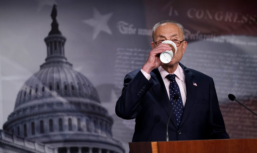 Senate Majority Leader Charles Schumer drinks a coffee at the podium