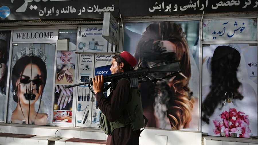 A Taliban fighter walks past a beauty saloon with images of women's faces defaced using black spray paint