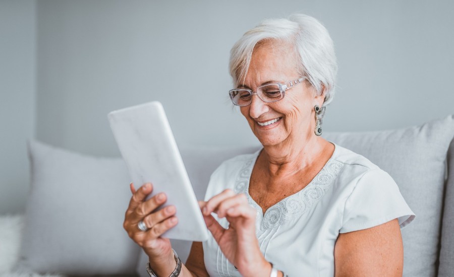 older woman smiling while using a tablet device