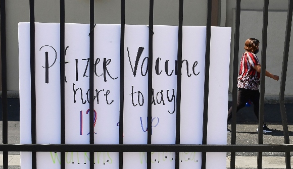 A woman walks past a sign announcing the Pfizer Covid-19 vaccine in use at a mobile vaccine clinic