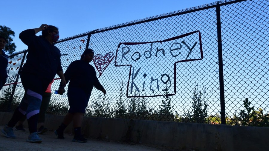 People walk past the name Rodney King seen on a chain-link fence