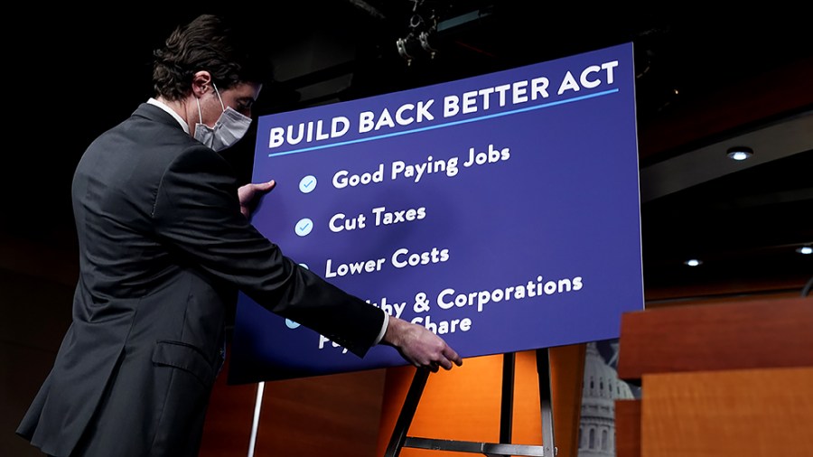 An aide for Speaker Nancy Pelosi (D-Calif.) places a chart for the Build Back Better Act prior to her weekly on-camera press conference on Thursday, November 18, 2021.