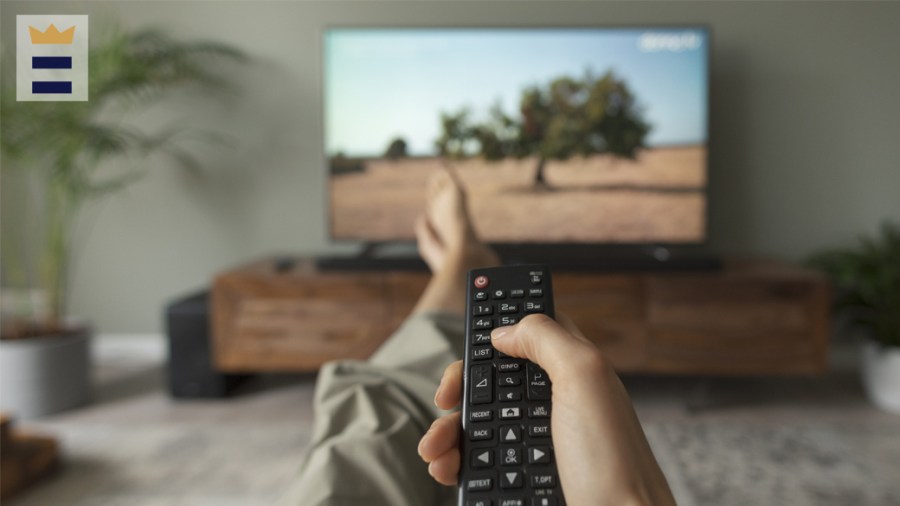 A hand points a remote control to a TV screen.