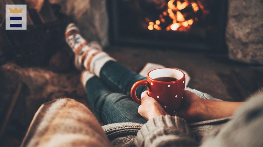 Person sits in front of a fireplace, holding a red mug.