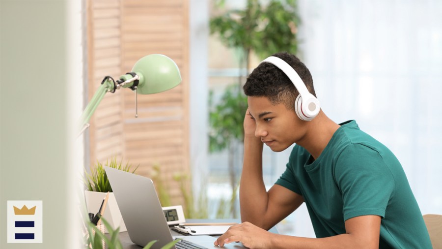 Teenager wears white wireless headphones while using a laptop.