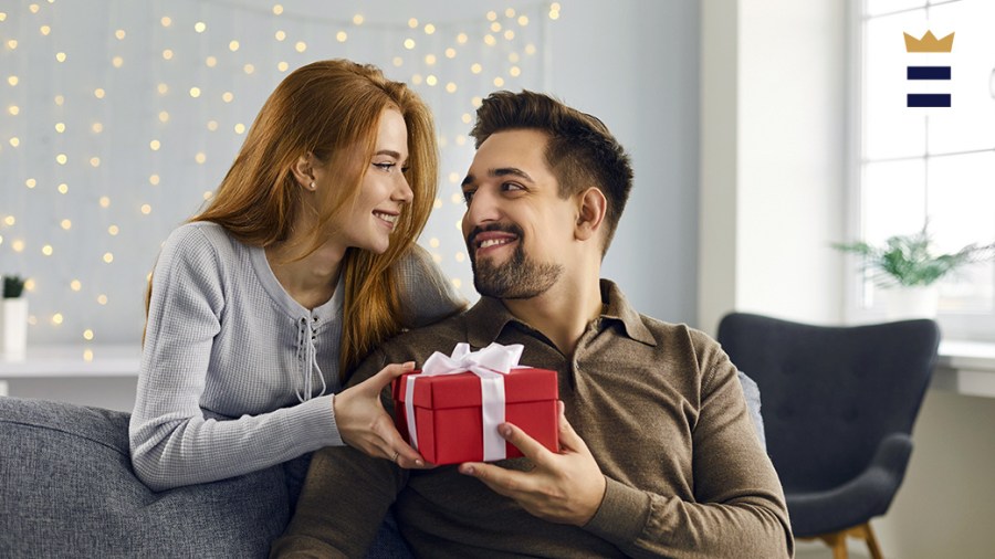 A couple smiles at each other while holding a red gift.