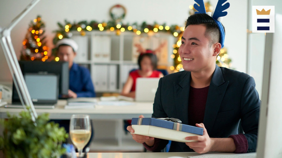 Smiling employee wearing blue antlers holds a gift at a holiday party.