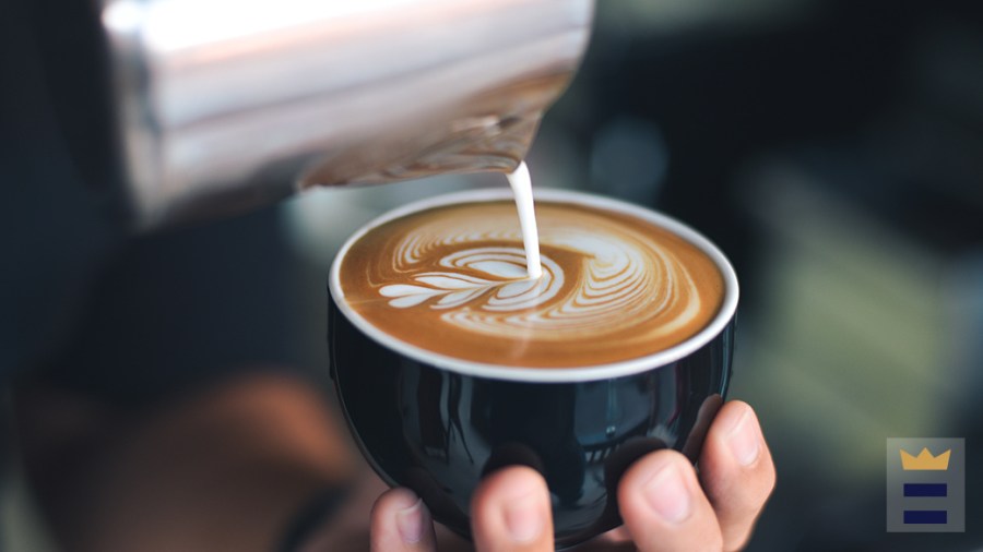 Hand holding a mug of coffee while someone pours cream into the mug.