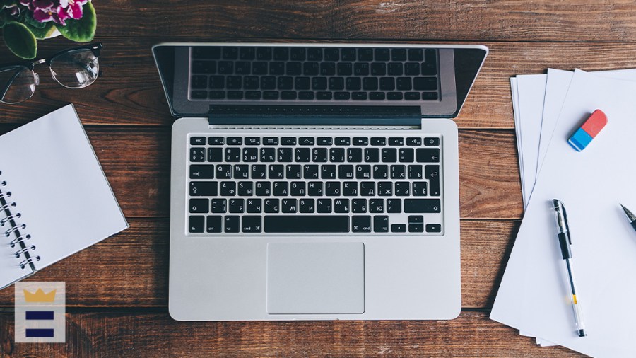 Laptop sitting between notebook and bank pieces of paper with pens and an eraser on top of them.