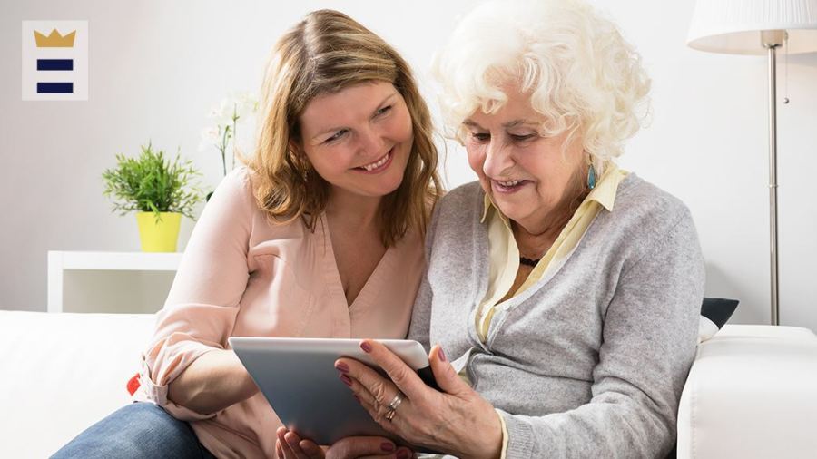 Two people sit on a couch, looking at a smart tablet.