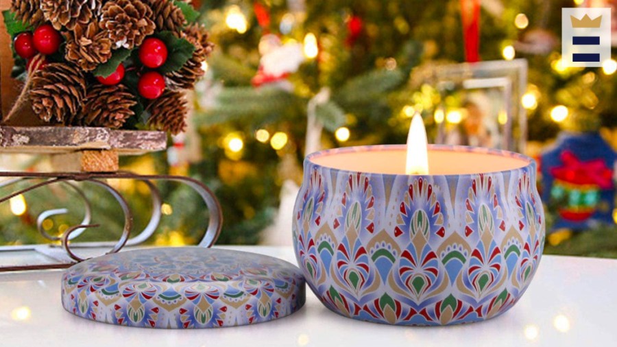 Lit candle sits next to a pinecone decoration and in front of a holiday tree.