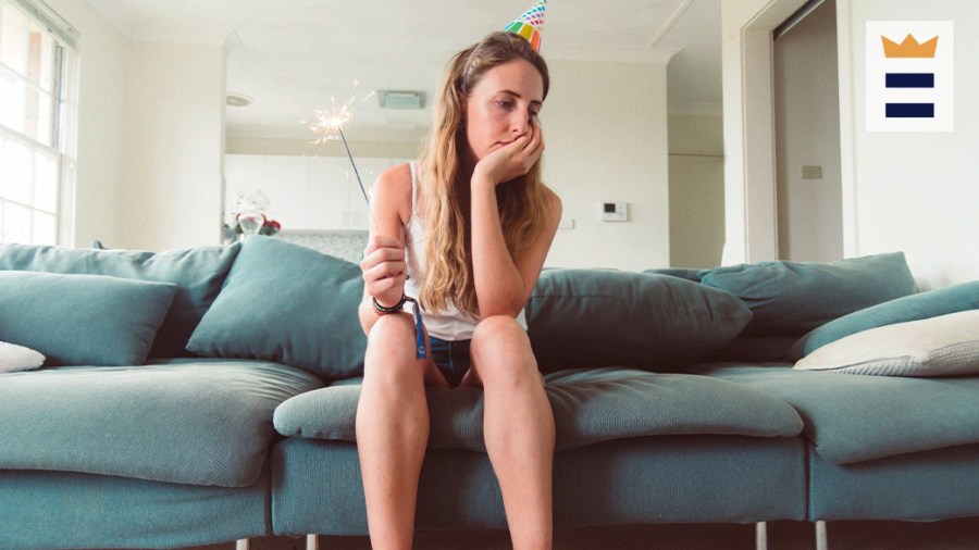 Woman sitting alone on her couch looking sad and holding a sparkler