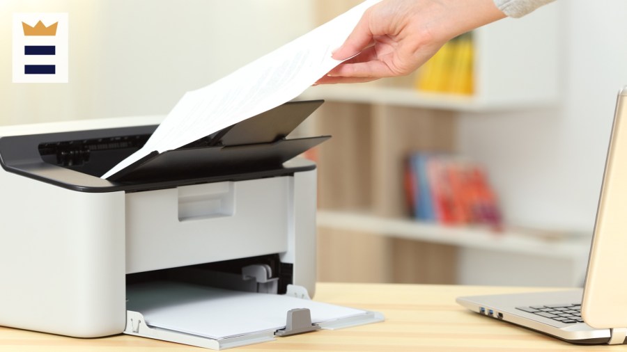 A hand pulls a piece of paper out of a printer.