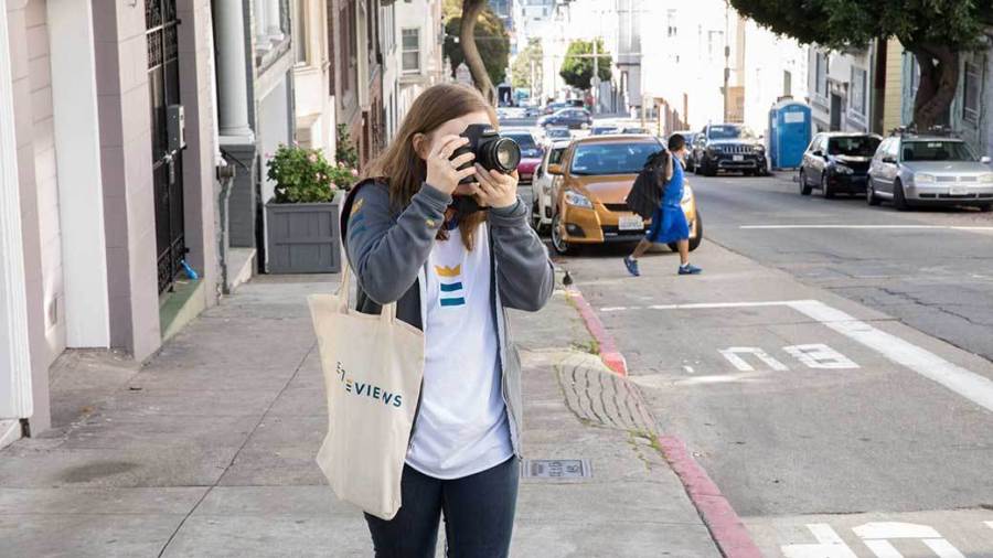 Person walks along the sidewalk, taking pictures with a mirrorless camera.