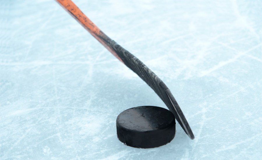 A hockey stick behind a puck on an ice rink