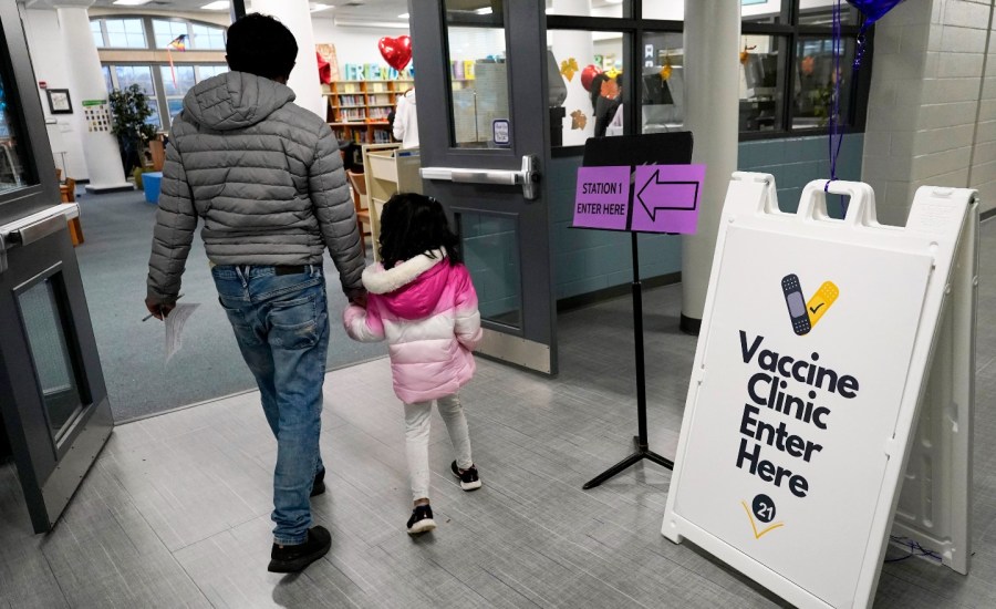 adult and child walk into a vaccine clinic with signage