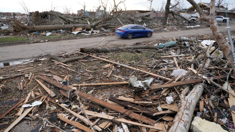 A car drives down a street lined with debris Saturday, Dec. 11, 2021, in Mayfield, Ky.