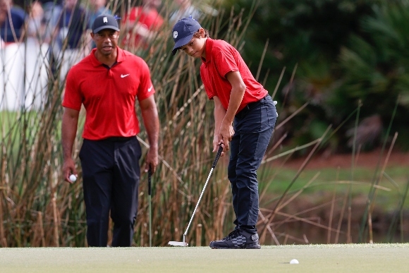 Charlie Woods sinks a putt on the second green while being watched by father Tiger Woods