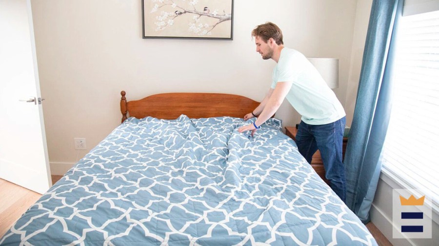 Man making up the bed with a blue and white bedspread