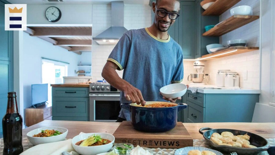 Man in a blue kitchen serving himself some food from a dark blue pot