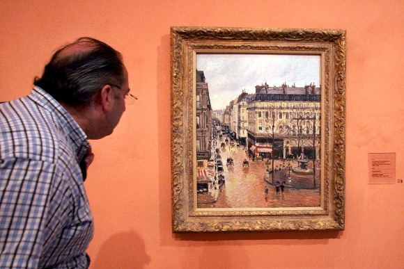 A visitor viewing the Impressionist painting called "Rue St.-Honore, Apres-Midi, Effet de Pluie" painted in 1897 by Camille Pissarro