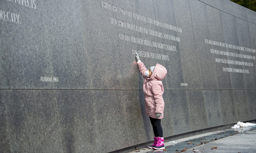 A girl in a pink hoodie reaches up to touch a quote from Martin Luther King Jr. at his memorial