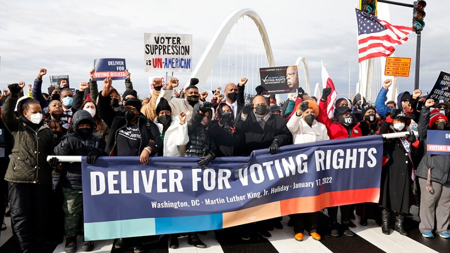 Protesters march in favor of increased protections for voting rights with a blue "Deliver Voting Rights" banner during Martin Luther King Jr. Day event.