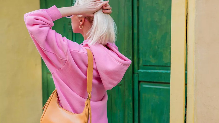 Woman with blond hair carrying an ochre purse standing in front of a yellow building with a green door